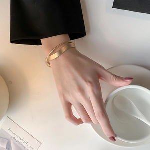 Bracciale a fascia incrociata in oro opaco indossato al polso per uno stile moderno