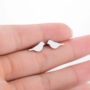 Polished silver stainless steel bird stud earrings shown for scale on a fingertip