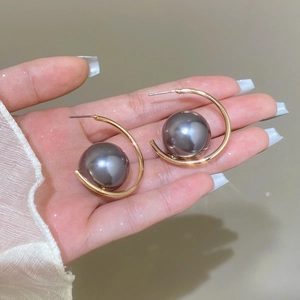 Macro detail of elegant C-shaped gold earrings with large dark grey pearl inlays