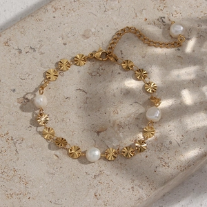 Detail of gold pearl bracelet with textured metal discs and lobster clasp on stone surface