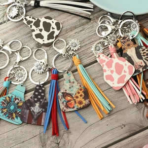 Western style cow tag keychains with sunflower charms and leather tassels on wood surface