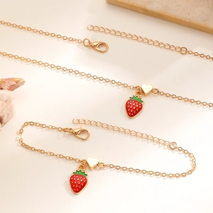 Dettaglio del set collana e bracciale dorati con ciondoli a fragola e piccoli cuori