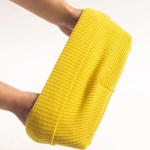 Bright yellow ribbed knit beanie showing high elasticity through hand stretching test