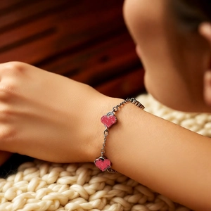 Detail of silver chain bracelet with red heart charms on a white knit blanket