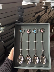 Close-up of four stainless steel dessert spoons with star and moon pendants in a gift box