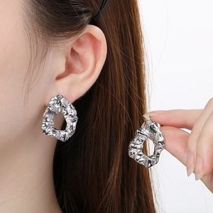 Close-up of silver irregular pleated earrings with textured lava-like surface on a model