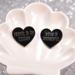 Pair of black heart enamel pins with slogan engraving on an elegant shell tray