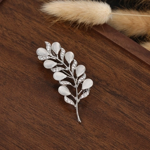 Macro detail of leaf-shaped brooch with white opals and clear rhinestones on wood
