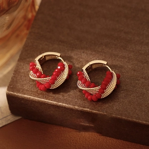 Detail view of twisted gold wire earrings with red crystal beads on a textured stand