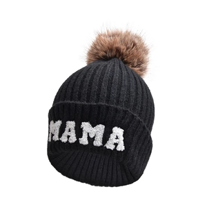 Dettaglio del berretto in maglia nera con ricamo MAMA e pompon in finta pelliccia marrone