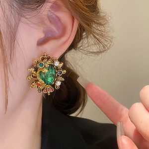 Close-up of vintage crown earrings with green gemstones and pearls on a model