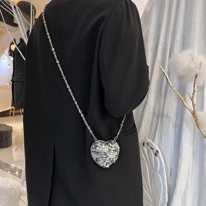 Silver heart-shaped sequin crossbody bag with chain strap shown on a black outfit