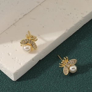 Elegant gold bee earrings with pearl abdomen and rhinestone wings on textured stone base