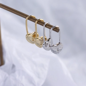 Detail of heart-shaped padlock earrings in gold and silver finish on white fabric