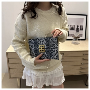 Detail view of leopard print clutch bag with golden H-shaped buckle on a white outfit