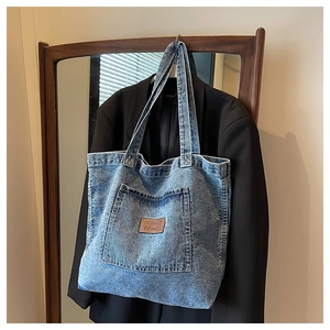 Detail of light blue washed denim tote bag showing leather logo and outer pocket detail