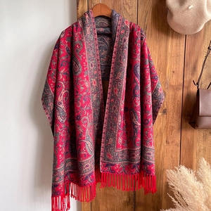Detail of red and blue paisley cashmere-like shawl with tassels on vintage wooden background