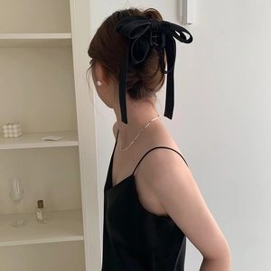 Elegant black silk bow hair clip worn in a half-up hairstyle by a model in a minimalist room