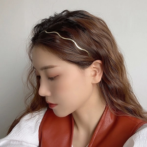 Minimalist gold wavy metal headband hair accessory worn by model against a white background