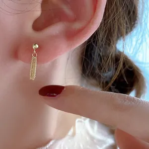 Close-up of gold tassel stud earring featuring delicate fine metal chains and a gold bead