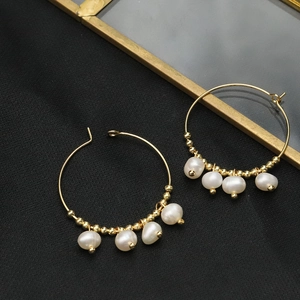 Elegant gold hoop earrings with irregular white pearls and beads on black background