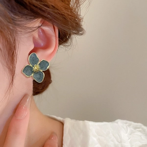 Detail view of a model wearing a grey-blue floral earring with golden metallic edges