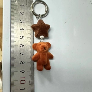 Detail shot of plush brown bear and star charm keychain with ruler for size measurement