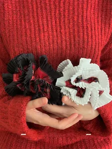 Detail of two plaid scrunchies with pleated lace edges held against a red sweater
