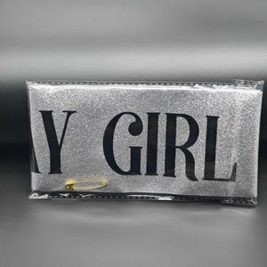 Close-up of silver glitter sash with Y GIRL text and gold safety pin in packaging