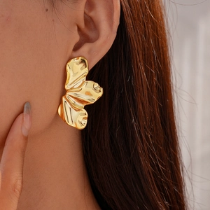 Detail of artistic gold leaf-shaped earrings with liquid metal texture on a model
