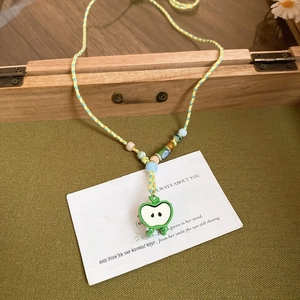 Macro detail of hand-woven cotton cord necklace with green apple pendant and colorful beads