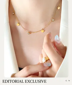 Close-up of gold necklace with heart charms and zircon ring on model in a white blazer