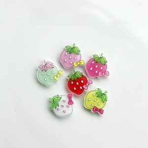 Macro detail of strawberry DIY resin charms with colorful bows on white surface