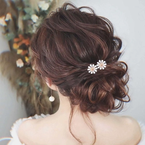Détail de deux épingles à cheveux marguerites blanches avec centre doré sur coiffure