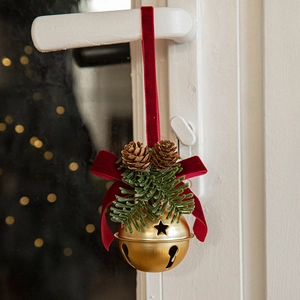 Christmas red velvet bow with gold bell and pine cones hanging on white door