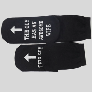 Black cotton socks with white text reading THIS GUY HAS AN AWESOME WIFE in flat lay view
