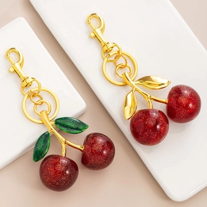 Sparkly red cherry keychain with gold leaves on a white tray, cute handbag accessory