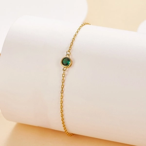 Detail of elegant gold bracelet with a round bezel-set green gemstone on minimalist stand