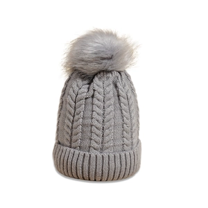 Detail of grey cable knit beanie with large faux fur pom-pom and thick ribbed cuff