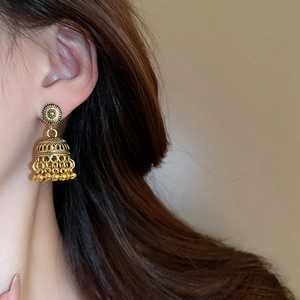 Macro shot of vintage gold Jhumka earrings with hollow carvings and beaded tassels