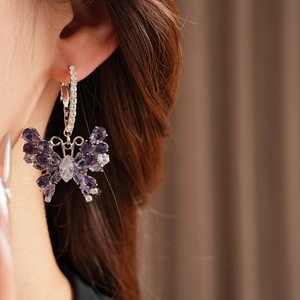 Close-up of a silver butterfly hoop earring with purple stones worn by a model