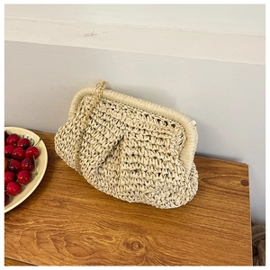 Detailed texture of beige woven straw clutch bag with gold chain strap on wood