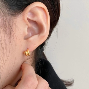 Close-up of model wearing gold-plated crossover hoop earrings in minimalist style