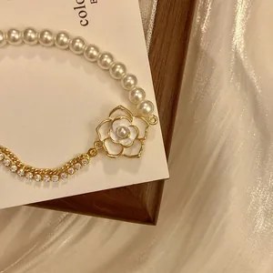 Detail view of pearl bracelet with diamond-encrusted camellia flower charm and gold chain