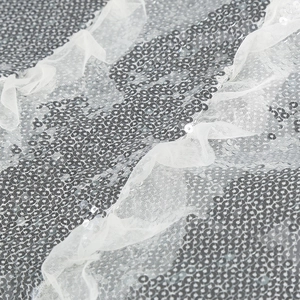 Close-up of silver sequin fabric with white lace ruffle details on a formal gown