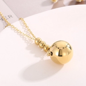 Detail einer minimalistischen Goldkugel-Halskette auf weißer Keramikoberfläche