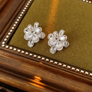 Dettaglio orecchini a fiore in argento con zirconi su superficie in tessuto verde