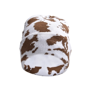 Close-up of thick knitted cow print beanie with textured brown spots on white fabric