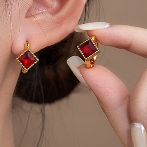 Close-up of vintage golden hoop earrings featuring square red crystal and beaded texture