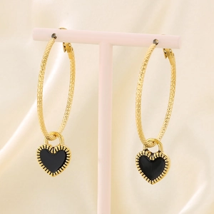 Detail of gold hoop earrings featuring black enamel heart charms on a pink jewelry stand